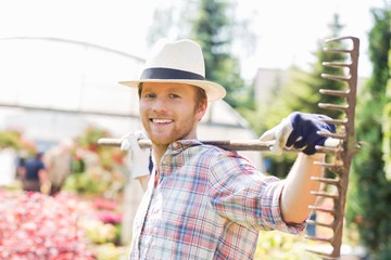 Portrait of smiling gardener carrying rake on shoulders at plant nursery