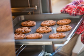 Cropped image of hand removing cookie tray from oven in kitchen