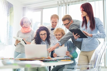 Smiling creative businesspeople working on laptop at desk in office