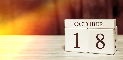 Calendar reminder event concept. Wooden cubes with numbers and month on October 18 with sunlight.