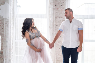 Pregnant couple in studio posing on abstract background. Husband looking tenterly on her wife waiting for a baby