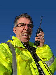 Man in green jacket shouts into walkie talkie