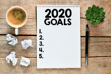 Top view 2020 new years goals list with notebook and coffee cup on wooden table.