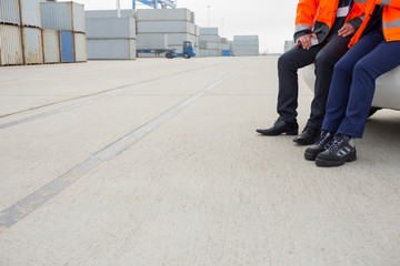 Low section of workers leaning on car in shipping yard