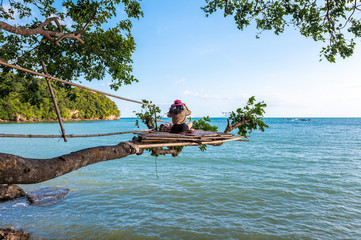 A woman sitting on a branch on tree in sea at Railay beach, Krabi, Thailand