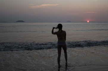 a girl coming to the beach from the sea water on the background of the rising sun