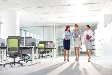 Full-length of businesswomen with file folders walking in office