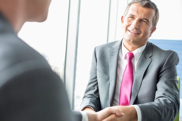 Smiling mature businessman shaking hands with partner in office