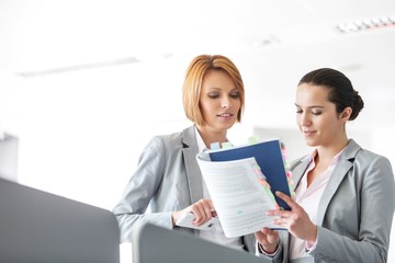 Young businesswomen discussing over book in office