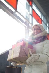 Smiling woman carrying stacked gifts during winter by window