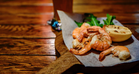 fried roasted shrimps with lemon and arugula on wooden table