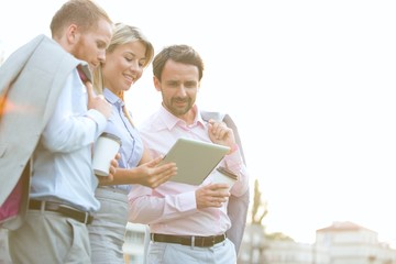 Low angle view of businesspeople using digital tablet against clear sky