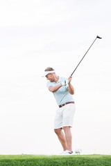 Full-length of mid-adult man swinging golf club against clear sky