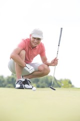 Smiling middle-aged man looking at ball while crouching on golf course