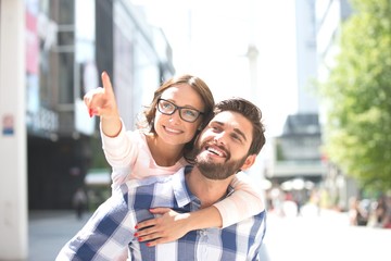 Cheerful woman pointing away while enjoying piggyback ride on man in city