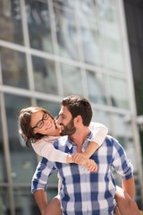 Happy couple looking at each other while enjoying piggyback ride in city