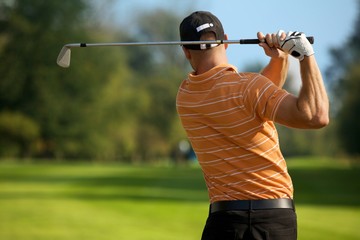Young man swinging golf club, rear view