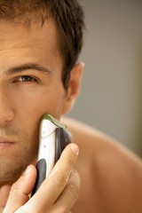 Reflection of young man in mirror shaving with electric shaver