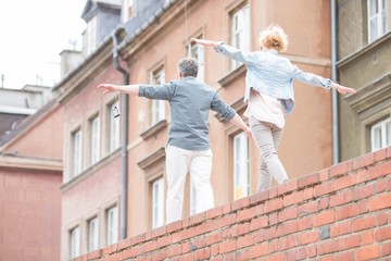 Rear view of middle-aged couple with arms outstretched walking on brick wall