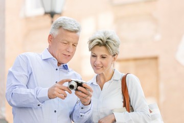 Smiling middle-aged couple reviewing photos on digital camera outdoors