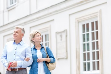 Smiling middle-aged couple standing with arm in arm outside building