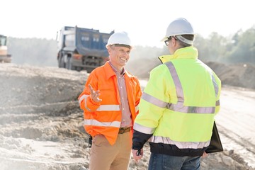 Happy engineer talking to colleague at construction site on sunny day