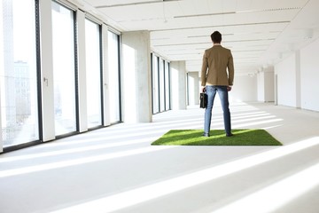 Full length rear view of young businessman standing on turf in empty office