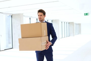 Young businessman carrying cardboard boxes in new office