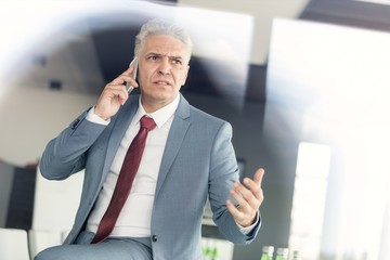 Serious mature businessman talking on mobile phone in office