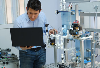 Focus on Engineer who is programming PLC with laptop for an analog process kit. Industry 4.0 workshop in an automation education center. Engineer is learning how to program a PLC.