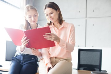 Young businesswomen reading file while sitting on desk in office