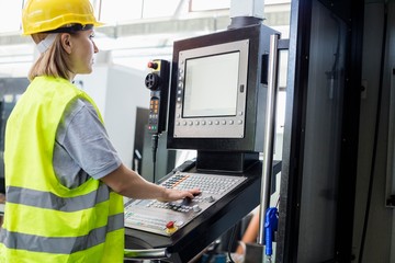 Side view of female worker operating machinery at control panel in factory