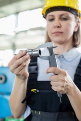 Mature female worker measuring metal with caliper in factory