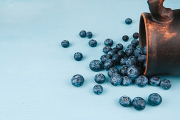  A bunch of ripe blueberries on a blue background copy space. Blueberries spilling out of a stein.