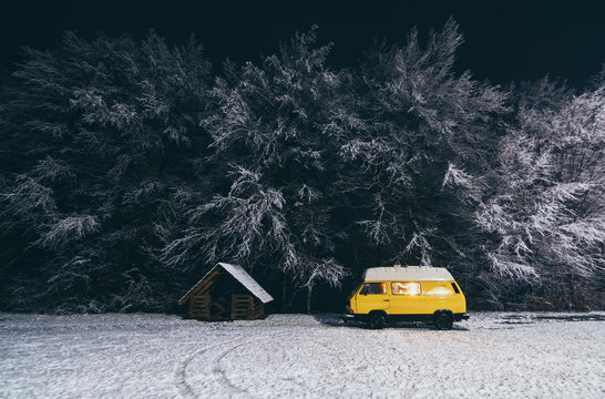 Yellow camper van with winter forest on background at night in Carpathians, Ukraine