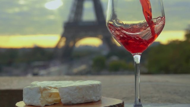 Red wine is poured into a glass next to Camembert cheese on the background of the Eiffel Tower, Paris, France