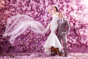 Full length of wedding couple standing against wall covered with pink flowers