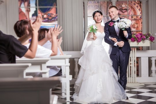 Wedding guests applauding for newlywed couple holding flowers in church