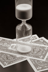 Dollar bills lie near the hourglass. Time is money. The salary. Business solutions in time....