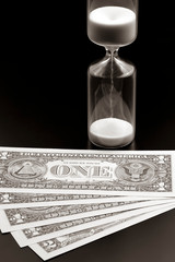 Dollar bills lie near the hourglass. Time is money. The salary. Business solutions in time....