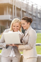 Happy young businesswomen using laptop together against building