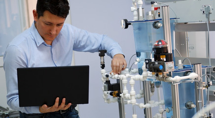 Focus on Engineer who is programming PLC with laptop for an analog process kit. Industry 4.0 workshop in an automation education center. Engineer is learning how to program a PLC. © Ridvan