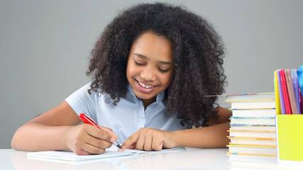 black school girl writes in a notebook, doing homework.