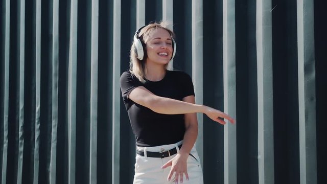smiling girl listens to music on headphones and dances on a background of black walls