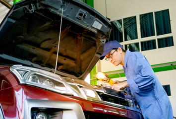 Asian automotive mechanic with blue uniform use lamp and wrench to fix the problem of the car in...