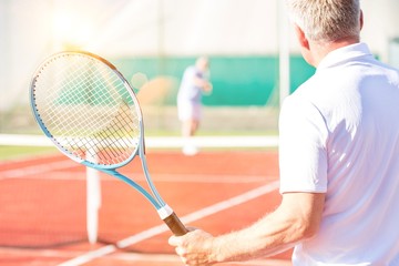 Rear view of mature man holding racket while playing with friend on tennis court