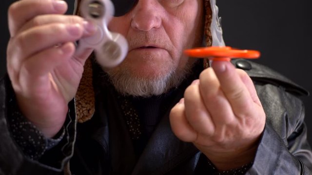 Portrait of strange elderly man spinning spiner on his nose. fancy pensioner with gray beard and black blindfold. bizarre people. 4K. Soothing toy. Autism. Senile memory loss, falling into childhood