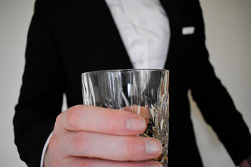 A close up view of a man in a black tuxedo cheersing with a whiskey glass