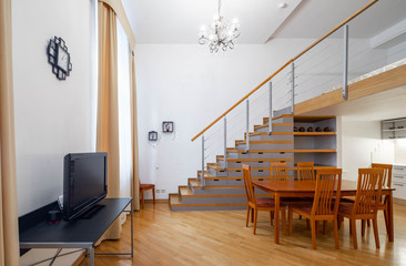 Interior in warm tones. Private house. Staircase to the second floor. Table and chairs.