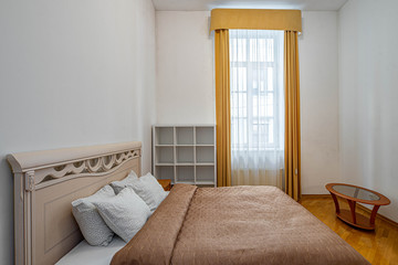 View of bed and window with curtain in bedroom interior. White walls.